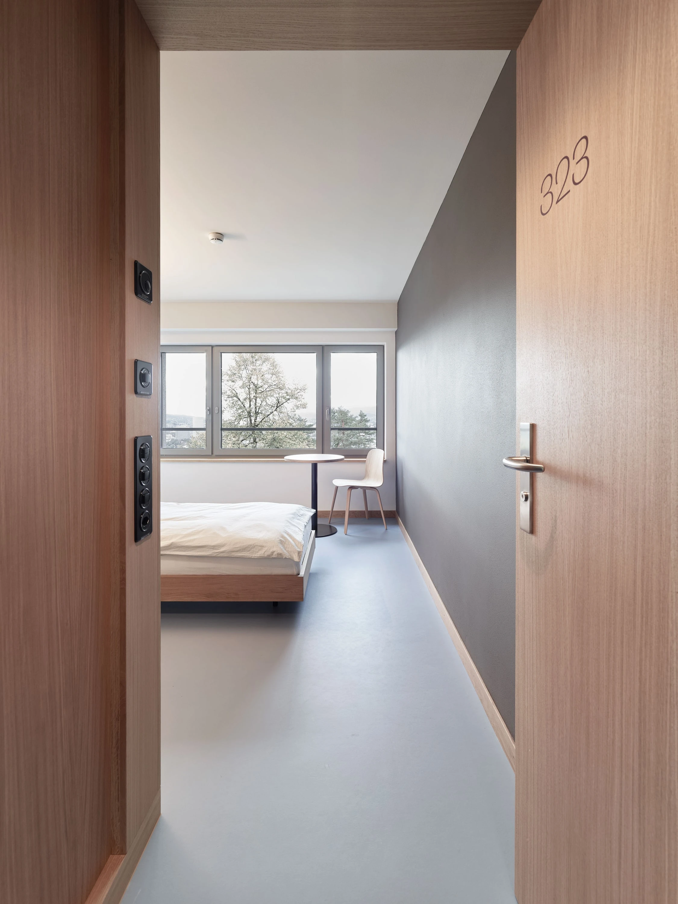 Blick durch eine offene Holztür in ein Patientenzimmer mit Bett.