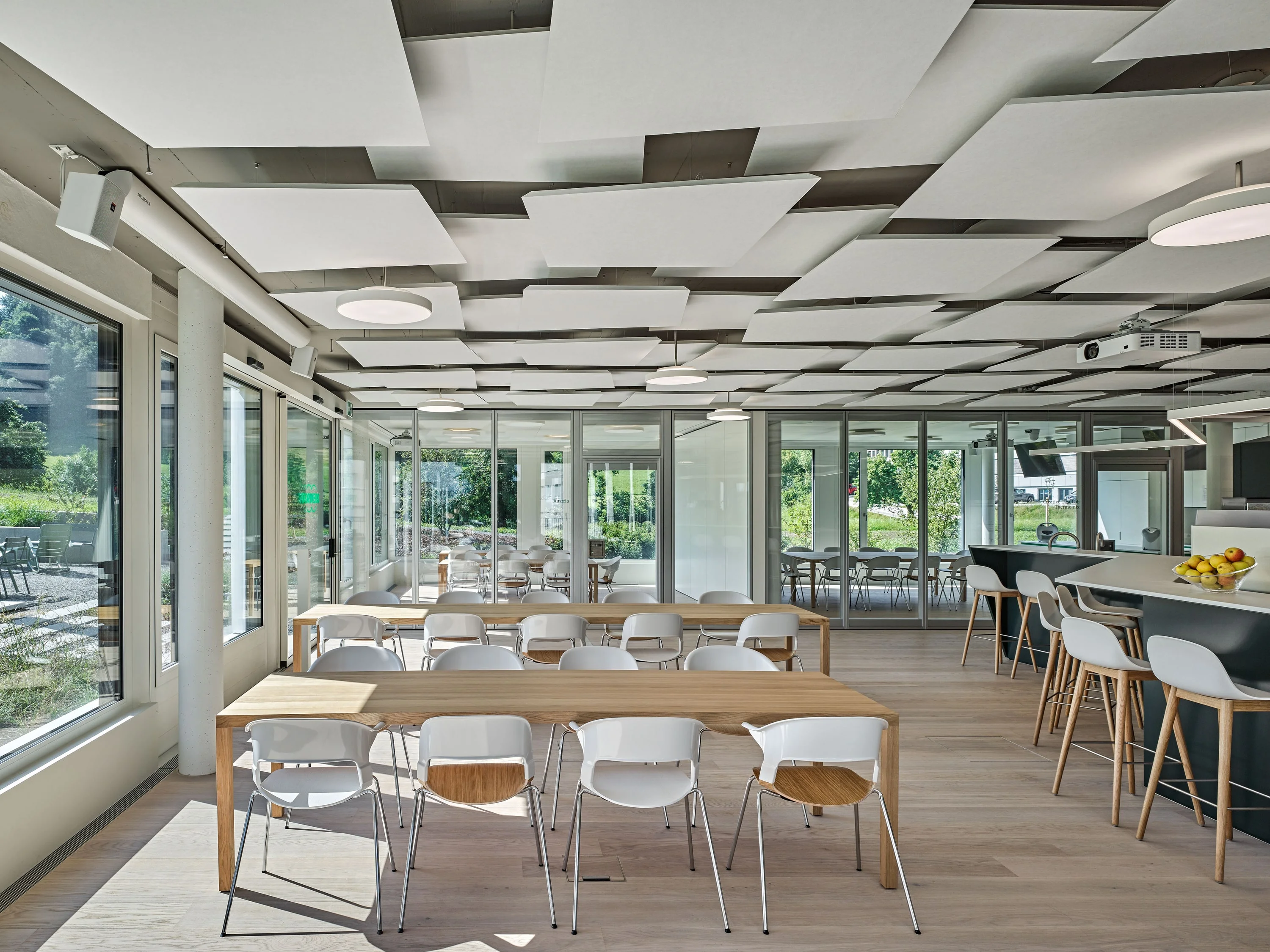 Betriebsrestaurant mit Holztischen, weissen Stühlen und Deckensegeln vor der Fensterfront.