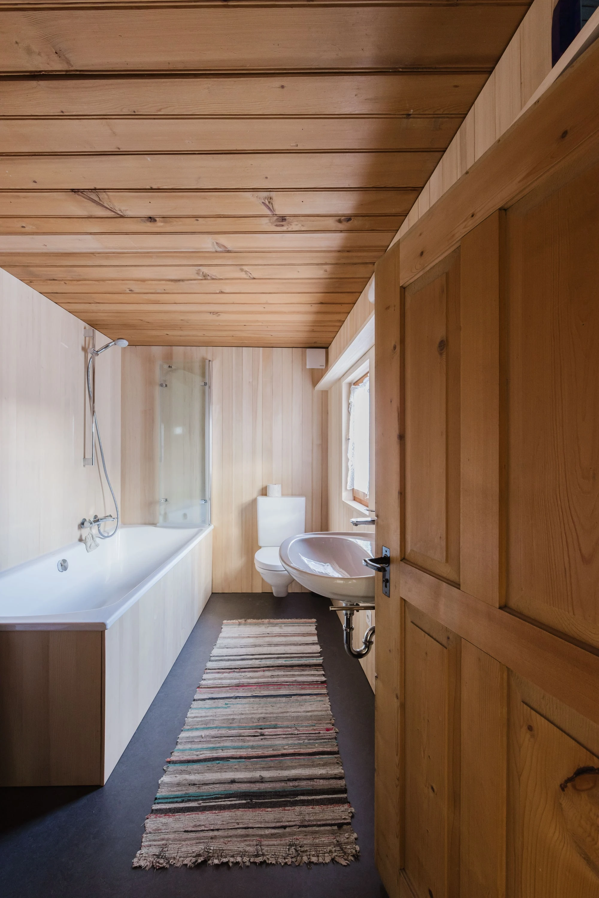 Bad mit Badewanne, Holztäfer und Läufer, gesehen durch die geöffnete Tür.