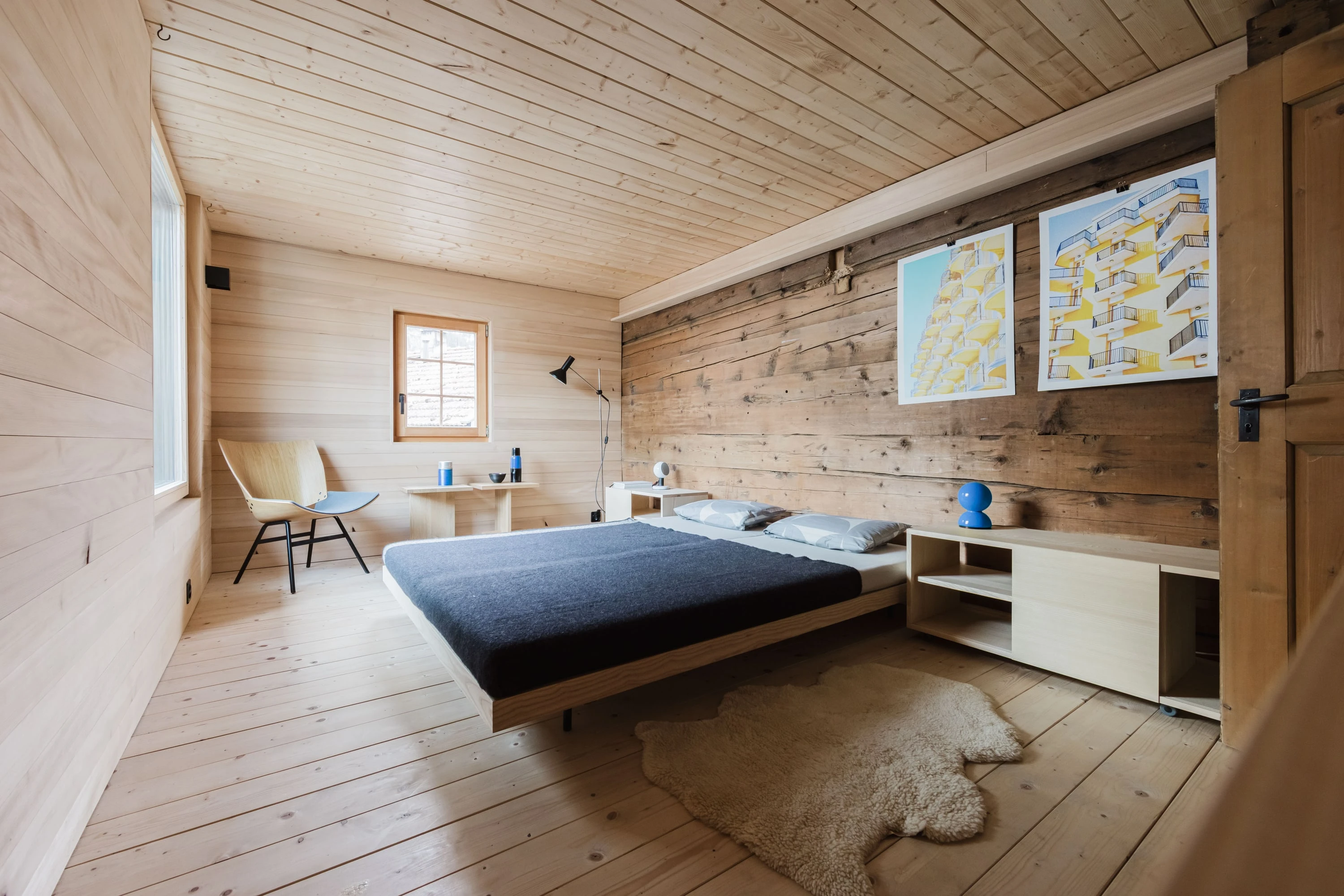 Grosses Zimmer mit altem Holztäfer, Bett, niedrigem Regal und Karten an der Wand.