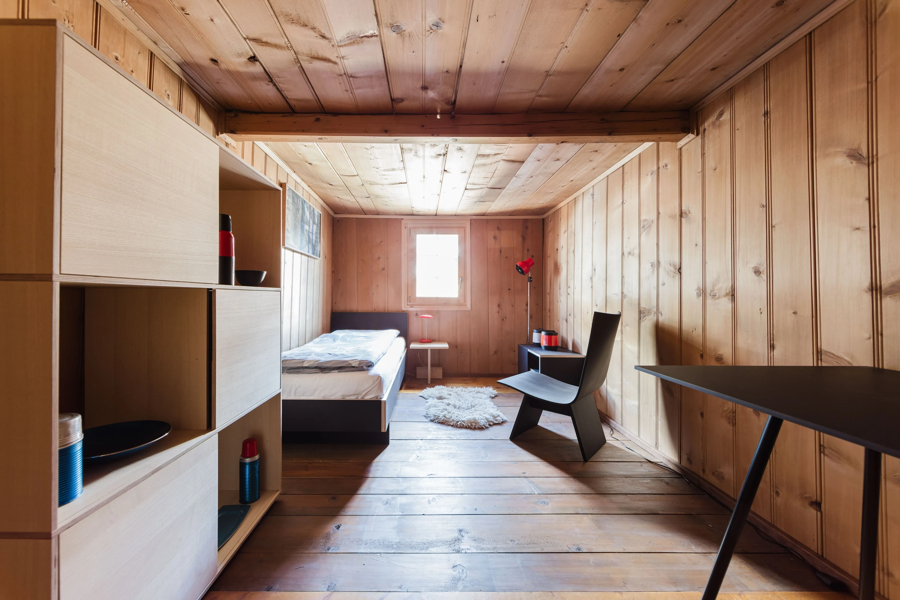 Kleines Zimmer mit altem Täfer, Bett, Stuhl und Regalwand.