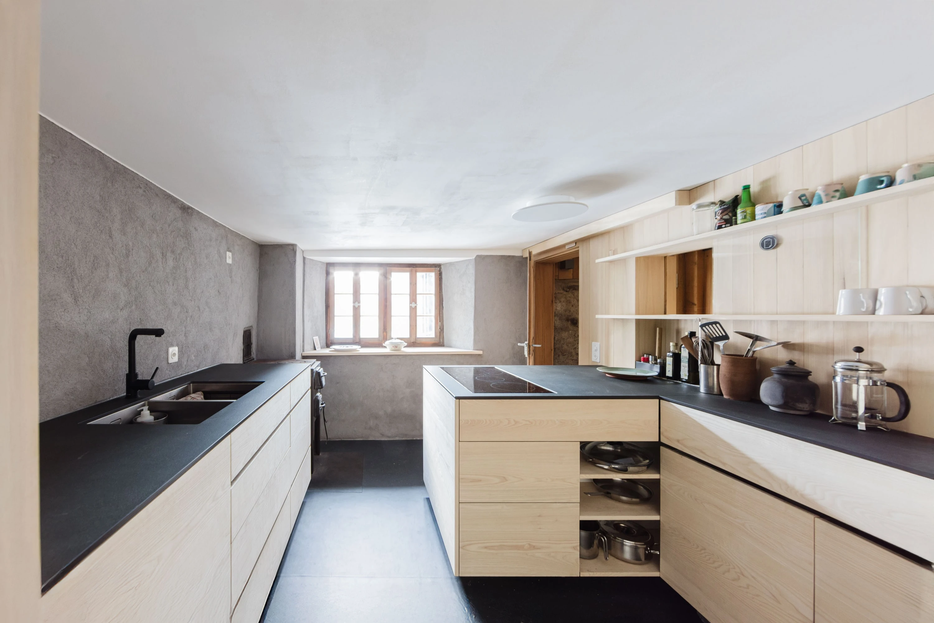 Küche mit Holzfronten, schwarzer Arbeitsplatte und Kücheninsel vor verputzter Wand.